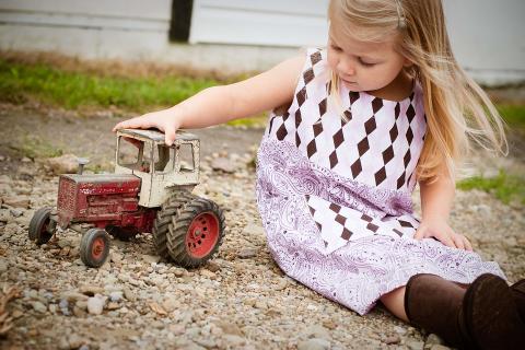 A toy tractor and a girl. The Thai for "a toy tractor and a girl" is "รถแทรกเตอร์ของเล่นและเด็กผู้หญิง".