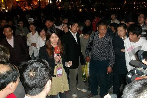 A female reporter and a crowd. The Thai for "a female reporter and a crowd" is "นักข่าวหญิงและกลุ่มคน".