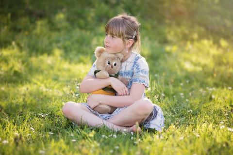 A girl and a teddy bear in a meadow. The Thai for "a girl and a teddy bear in a meadow" is "เด็กหญิงและตุ๊กตาหมีบนทุ่งหญ้า".