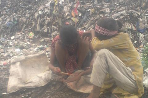 Two girls sitting on a pile of garbage. The Thai for "two girls sitting on a pile of garbage" is "เด็กหญิงสองคนนั่งบนกองขยะ".