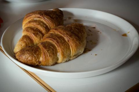 Two croissants on a white plate. The Thai for "two croissants on a white plate" is "ครัวซองส์สองชิ้นบนจานสีขาว".