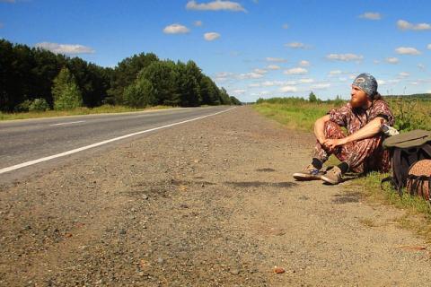 A man sits by the roadside. The Thai for "a man sits by the roadside" is "ผู้ชายนั่งข้างทาง".