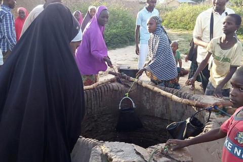 A group of people around a well. The Thai for "a group of people around a well" is "กลุ่มคนรอบบ่อน้ำ".