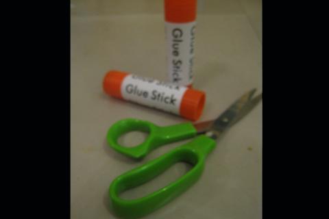 Two glue sticks and a pair of scissors. The Thai for "two glue sticks and a pair of scissors" is "กาวสองแท่งและกรรไกร".