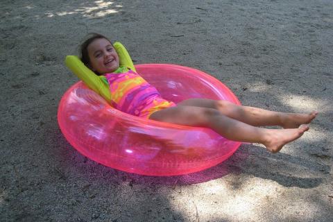 A girl is lying down on a pink rubber ring. The Thai for "a girl is lying down on a pink rubber ring" is "เด็กหญิงนอนบนห่วงยางสีชมพู".