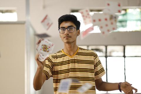 A magician throwing cards. The Thai for "a magician throwing cards" is "นักมายากลโยนไพ่".