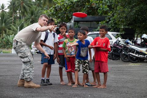 A soldier teaching children how to play frisbee. The Thai for "a soldier teaching children how to play frisbee" is "ทหารสอนเด็กๆเล่นจานบิน".