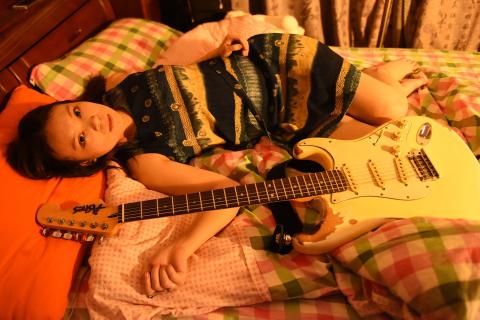 A woman and her guitar on a bed. The Thai for "a woman and her guitar on a bed" is "ผู้หญิงและกีตาร์ของเธอบนที่นอน".