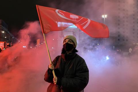 A female protester raises a red flag. The Thai for "a female protester raises a red flag" is "ผู้ประท้วงหญิงชูธงแดง".