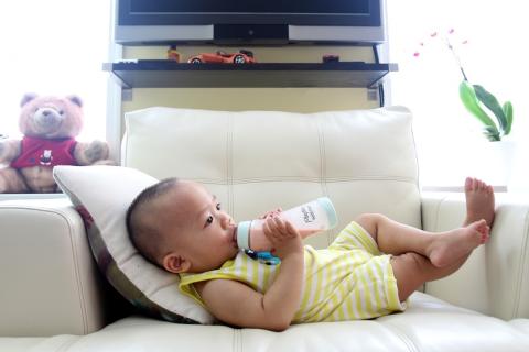 A baby with his bottle in an armchair. The Thai for "a baby with his bottle in an armchair" is "เด็กทารกกับขวดนมของเขาบนเก้าอี้นวม".