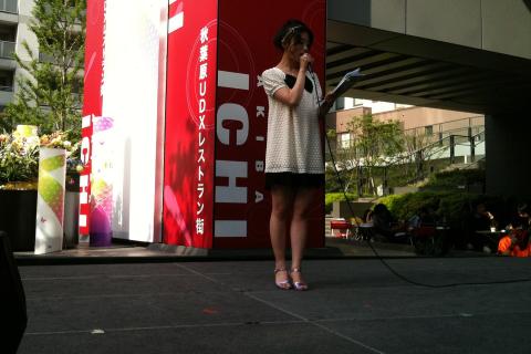 A female host on a stage. The Thai for "a female host on a stage" is "พิธีกรหญิงบนเวที".