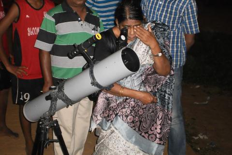 A woman looking through a telescope. The Thai for "a woman looking through a telescope" is "ผู้หญิงส่องกล้องดูดาว".
