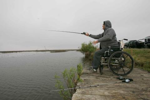 A man sitting in a wheelchair while fishing. The Thai for "a man sitting in a wheelchair while fishing" is "ผู้ชายนั่งอยู่ในวีลแชร์ขณะตกปลา".