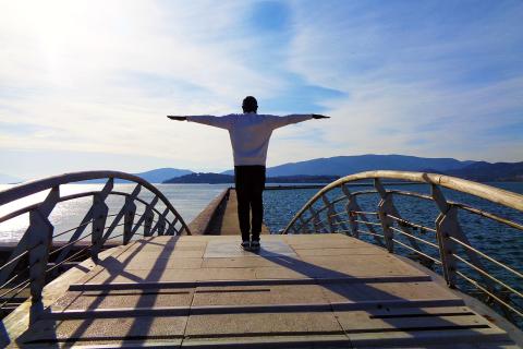 A man on a bridge standing with his arms outstretched. The Thai for "a man on a bridge standing with his arms outstretched" is "ผู้ชายยืนกางแขนบนสะพาน".