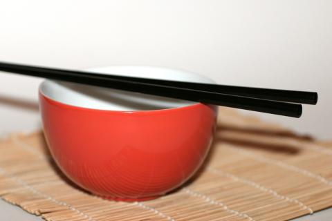 A pair of chopsticks on a red bowl. The Thai for "a pair of chopsticks on a red bowl" is "ตะเกียบหนึ่งคู่บนชามสีแดง".
